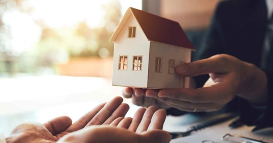 A person holding a miniature house and handing it off to another person