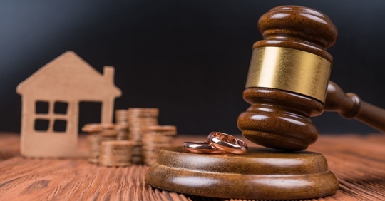 A gavel banging near two wedding rings, signifying division of a house and money