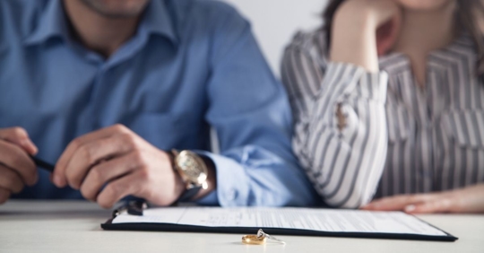 A man and woman sit at a desk together. Their wedding rings are off of their fingers.