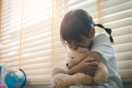 sad child hugging her teddy bear